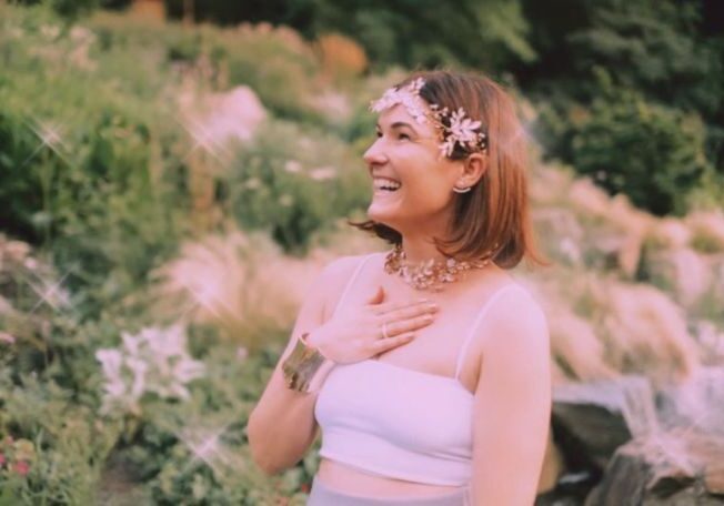 A woman wearing a white dress, smiling in a garden